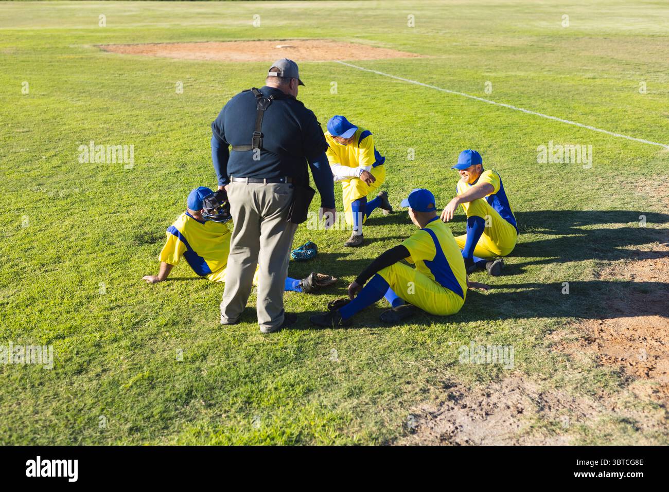 Entraîneur et joueurs de baseball adolescents masculins se rassemblant sur un diamant de terrain ensoleillé avec des gants et des casques Banque D'Images