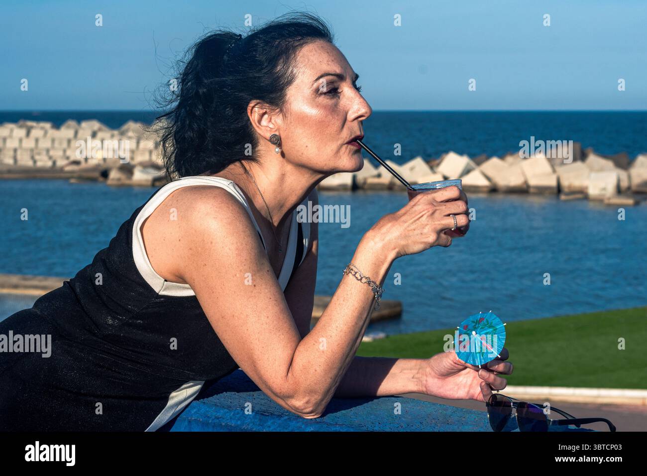 Modèle senior élégant profite d'une boisson colorée au bord de la mer, incarnant la positivité du corps et l'inclusion tout en mettant en valeur les joies de l'âge mûr Banque D'Images Modèle senior élégant profite d'une boisson colorée au bord de la mer, incarnant la positivité du corps et l'inclusion tout en mettant en valeur les joies de l'âge mûr Banque D'Images