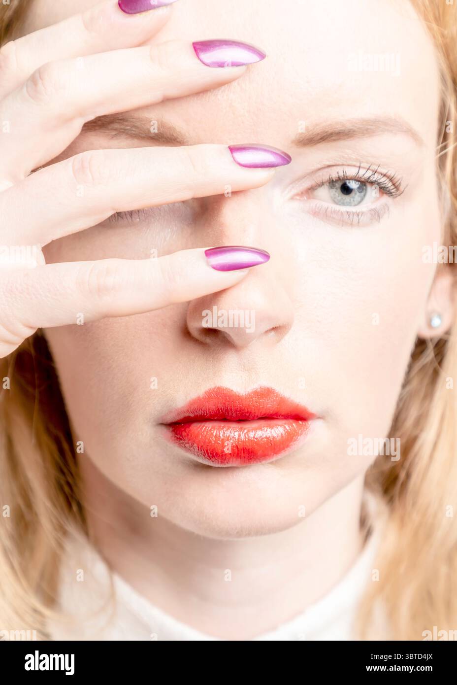 Une femme avec du rouge à lèvres rouge couvre ses yeux avec sa main, montrant son vernis à ongles violet. Banque D'Images