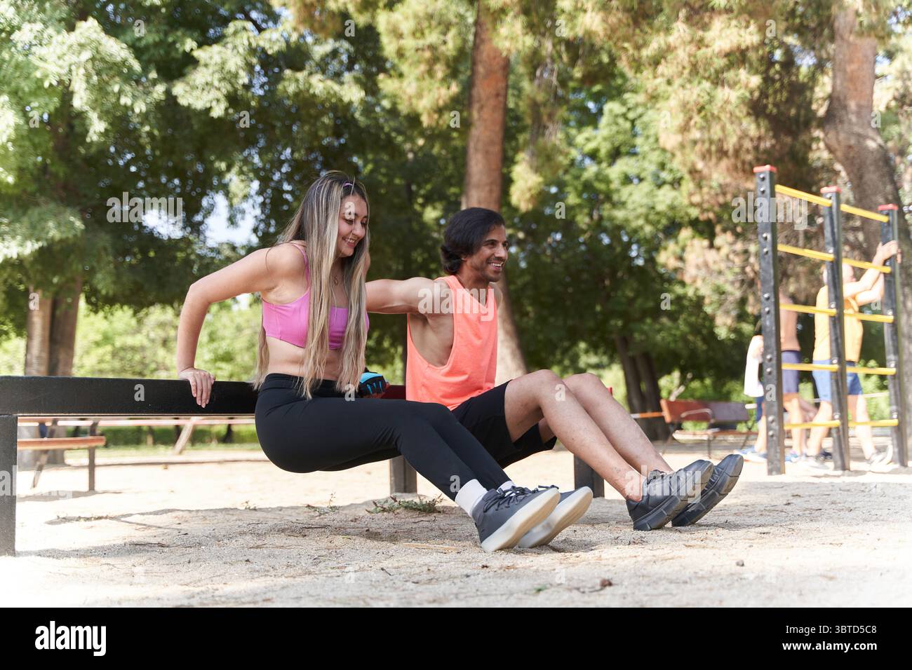 Couple de fitness effectuant des trempettes sur un banc dans un parc de calisthenics dynamique, profitant d'une journée ensoleillée tout en améliorant la force et la coordination Banque D'Images