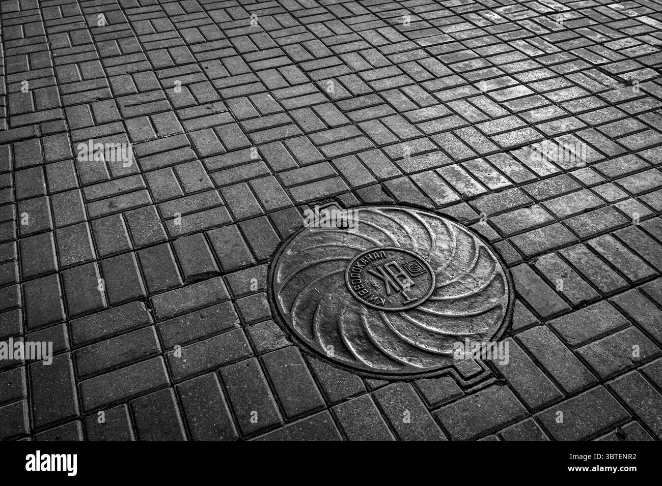 Couvercle de trou d'homme sur la rue pavée géométrique en noir et blanc Banque D'Images