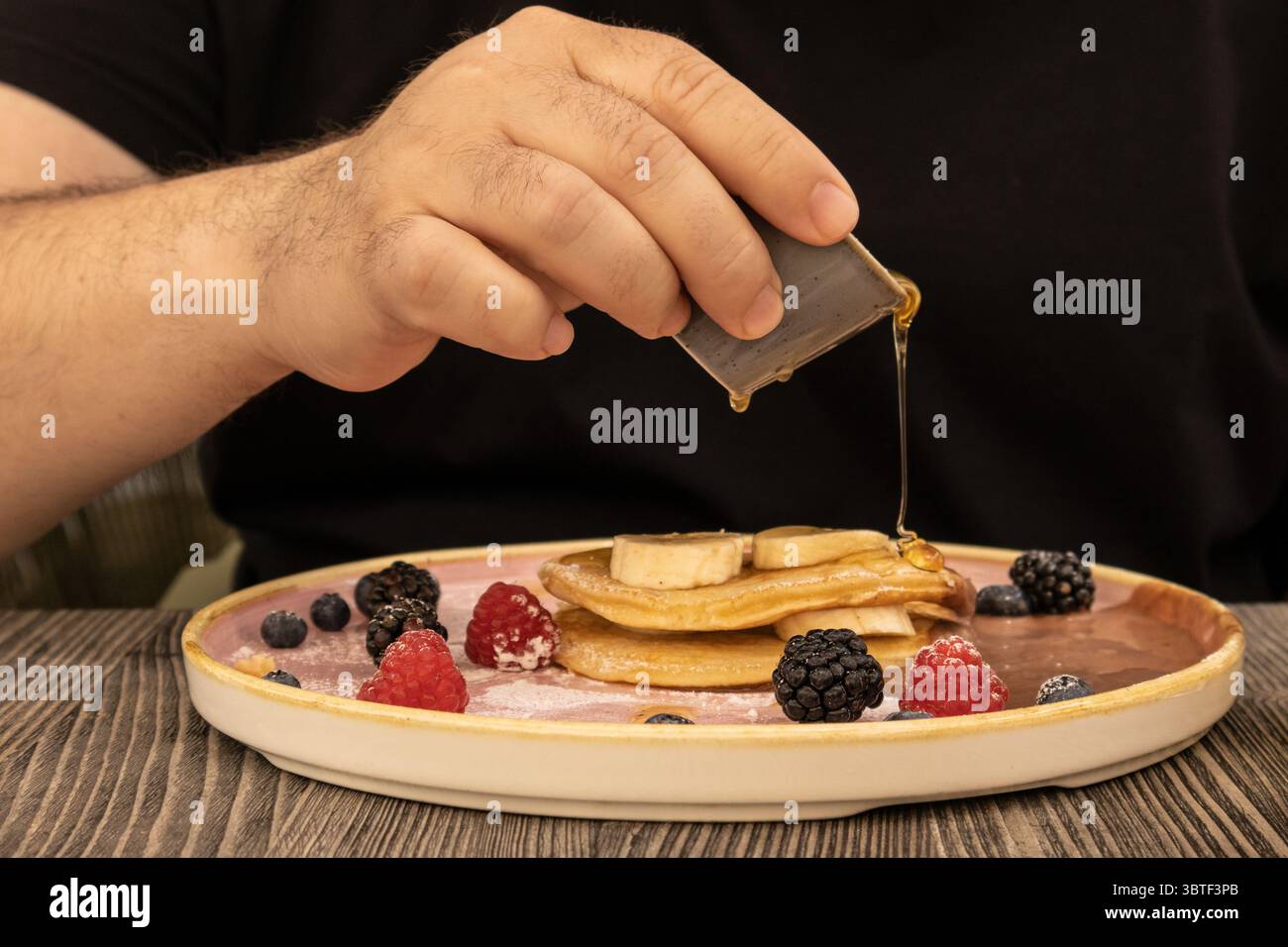 Gros plan d'un petit déjeuner copieux avec une pile de crêpes moelleuses garnies de baies fraîches et de sirop versé, évoquant le confort douillet et la détente. Banque D'Images