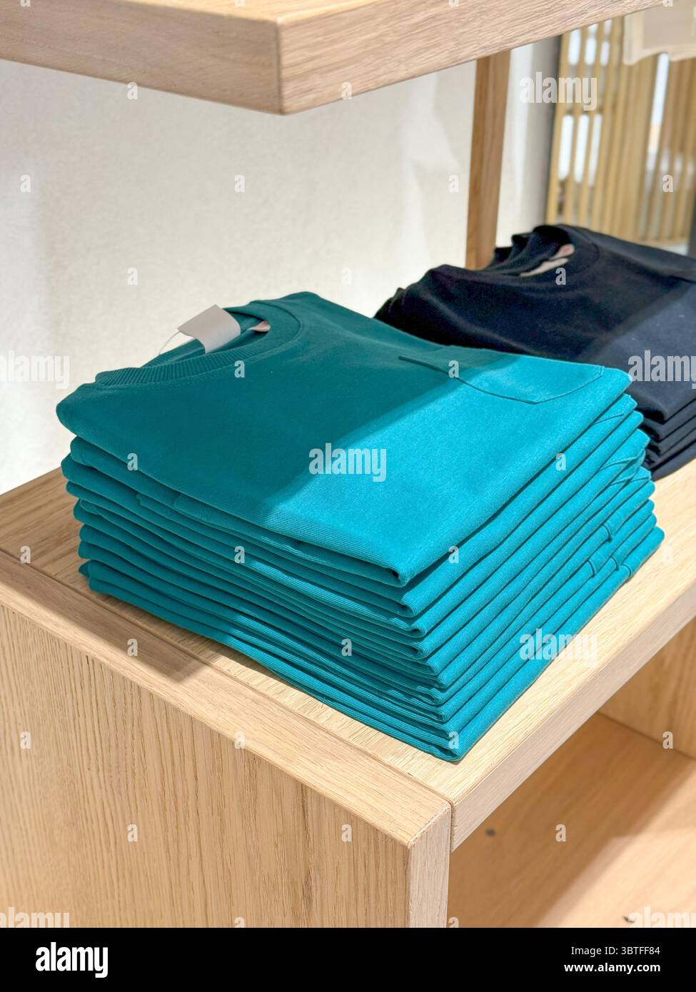 Chemises turquoise pliées sur l'étagère de vente au détail, pile soignée avec le contraste Earth-Tone Banque D'Images