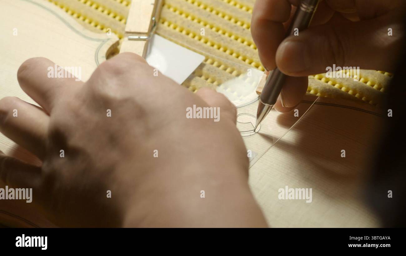 Gros plan des mains du luthier qui fabriquent méticuleusement un trou f sur la table d'harmonie d'un violoncelle, en utilisant un gabarit et un crayon avec précision et expertise dans un tra Banque D'Images