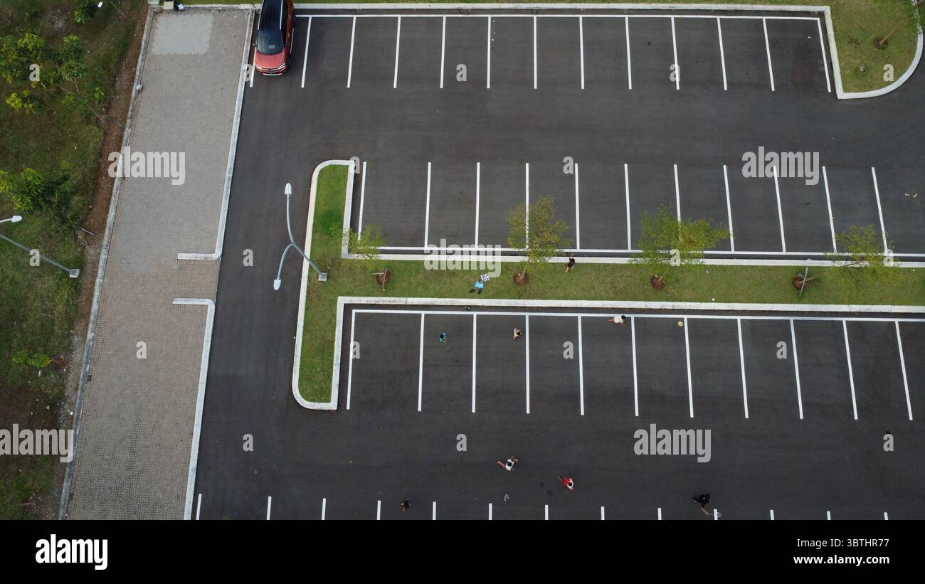 La vue aérienne présente un parking avec des espaces rayés, de la verdure et une voiture rouge solitaire, créant un paysage urbain. Banque D'Images