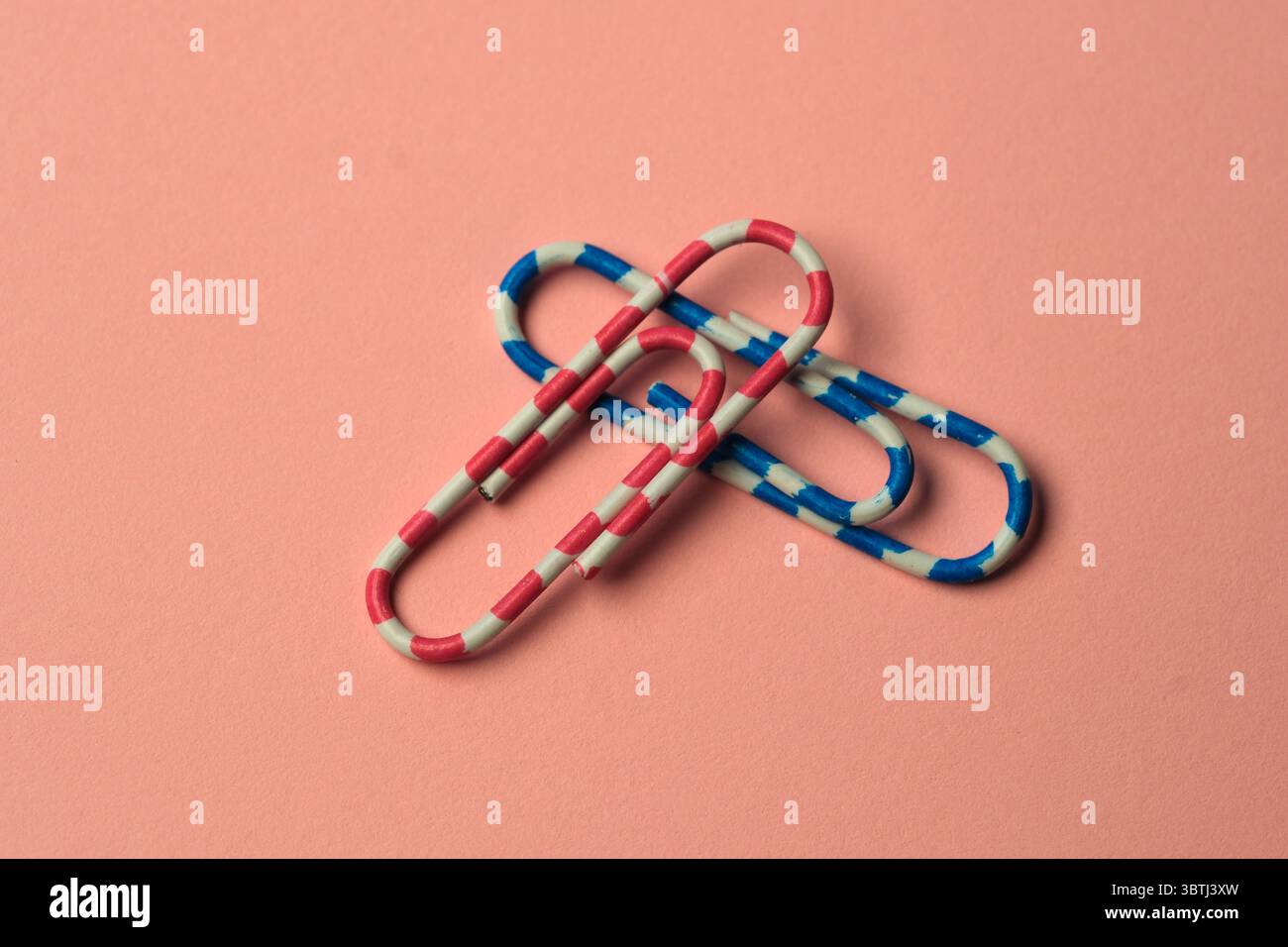 Les trombones aux couleurs vives s'entrelacent sur une surface pastel douce, créant ainsi des trombones Banque D'Images