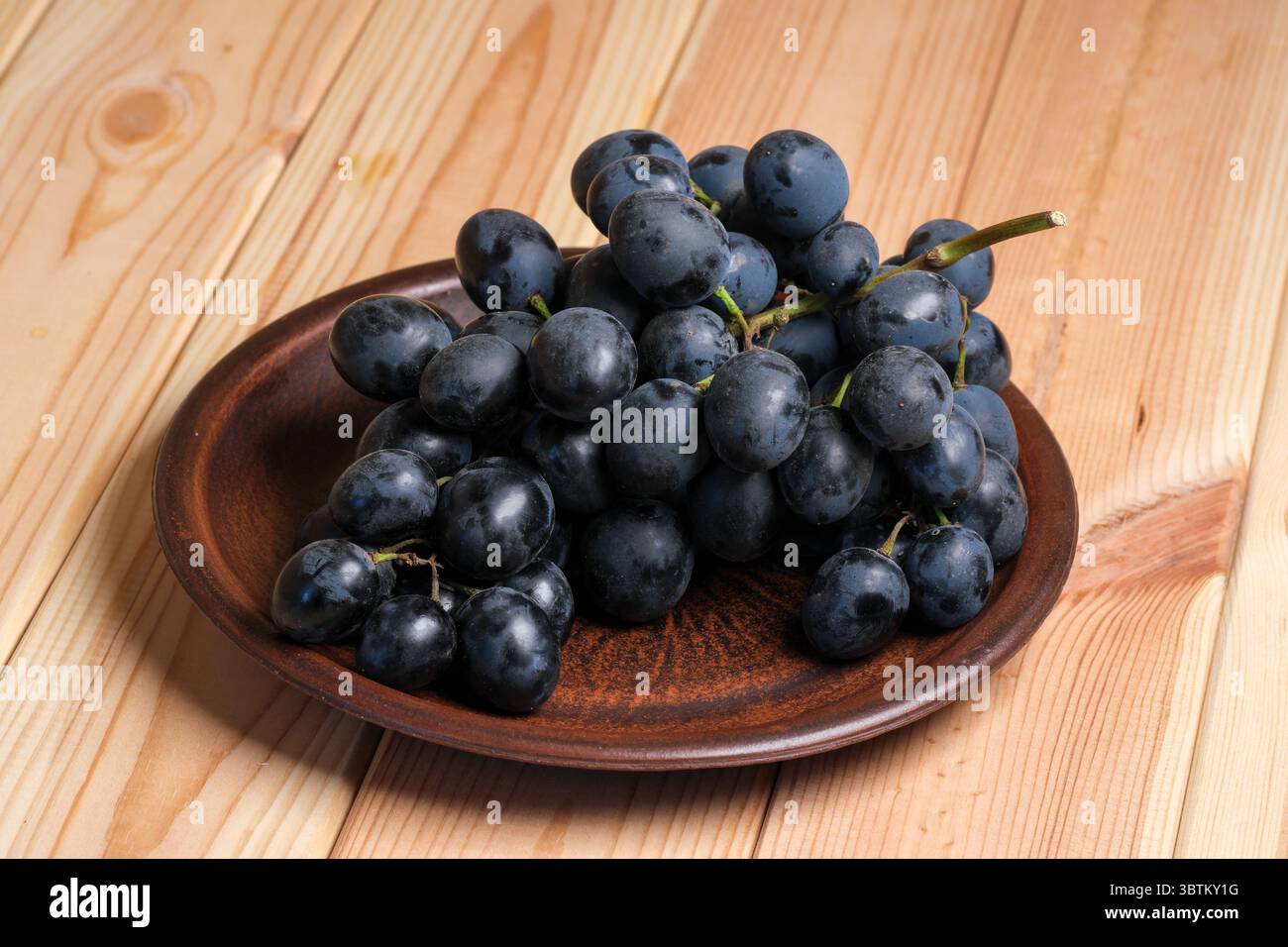 Raisins noirs mûrs doux non lavés avec de la cire naturelle sur la peau sur une table en bois clair gros plan Banque D'Images