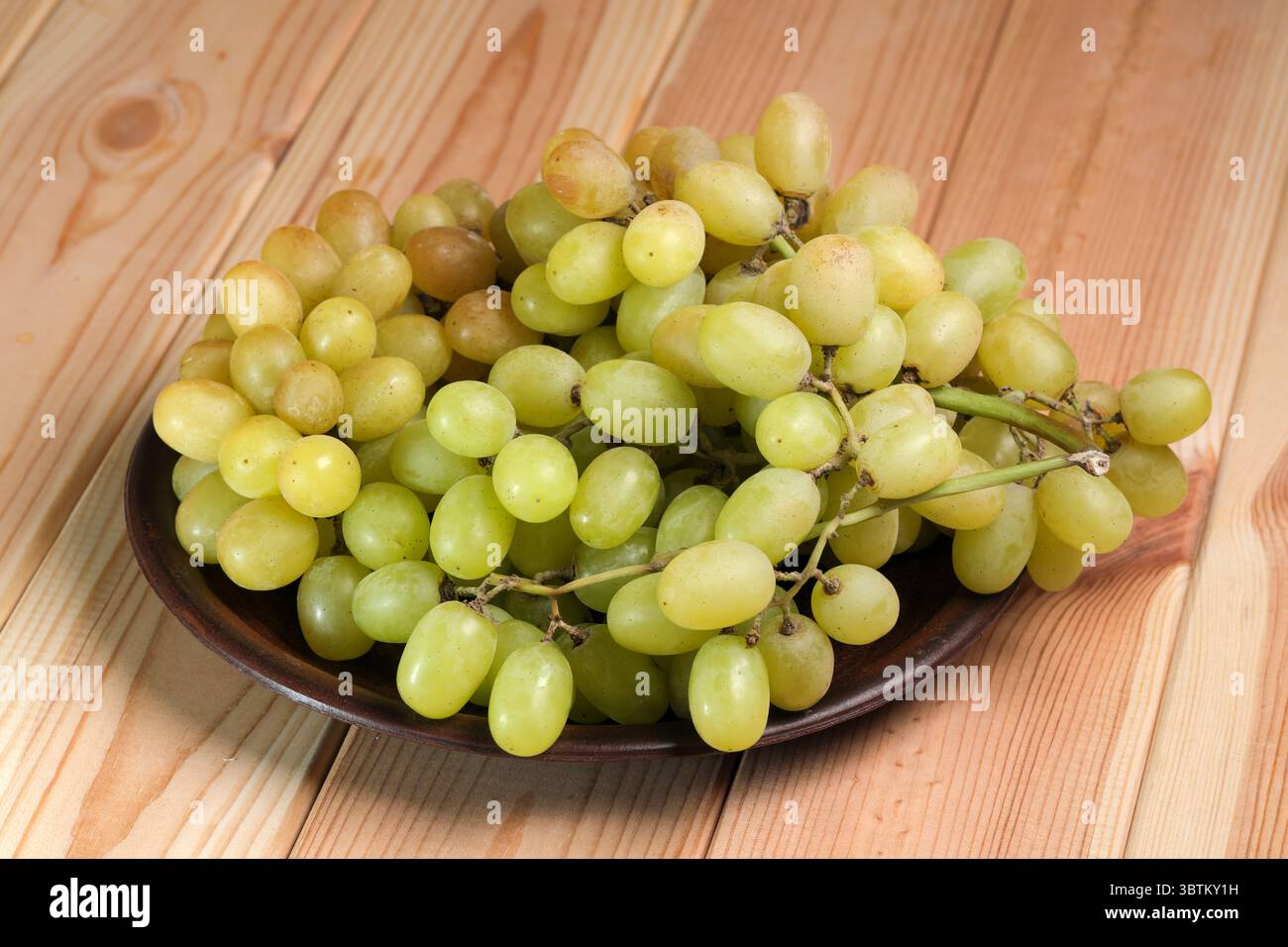 Raisins blancs mûrs doux non lavés avec de la cire naturelle sur la peau sur une table en bois clair gros plan Banque D'Images