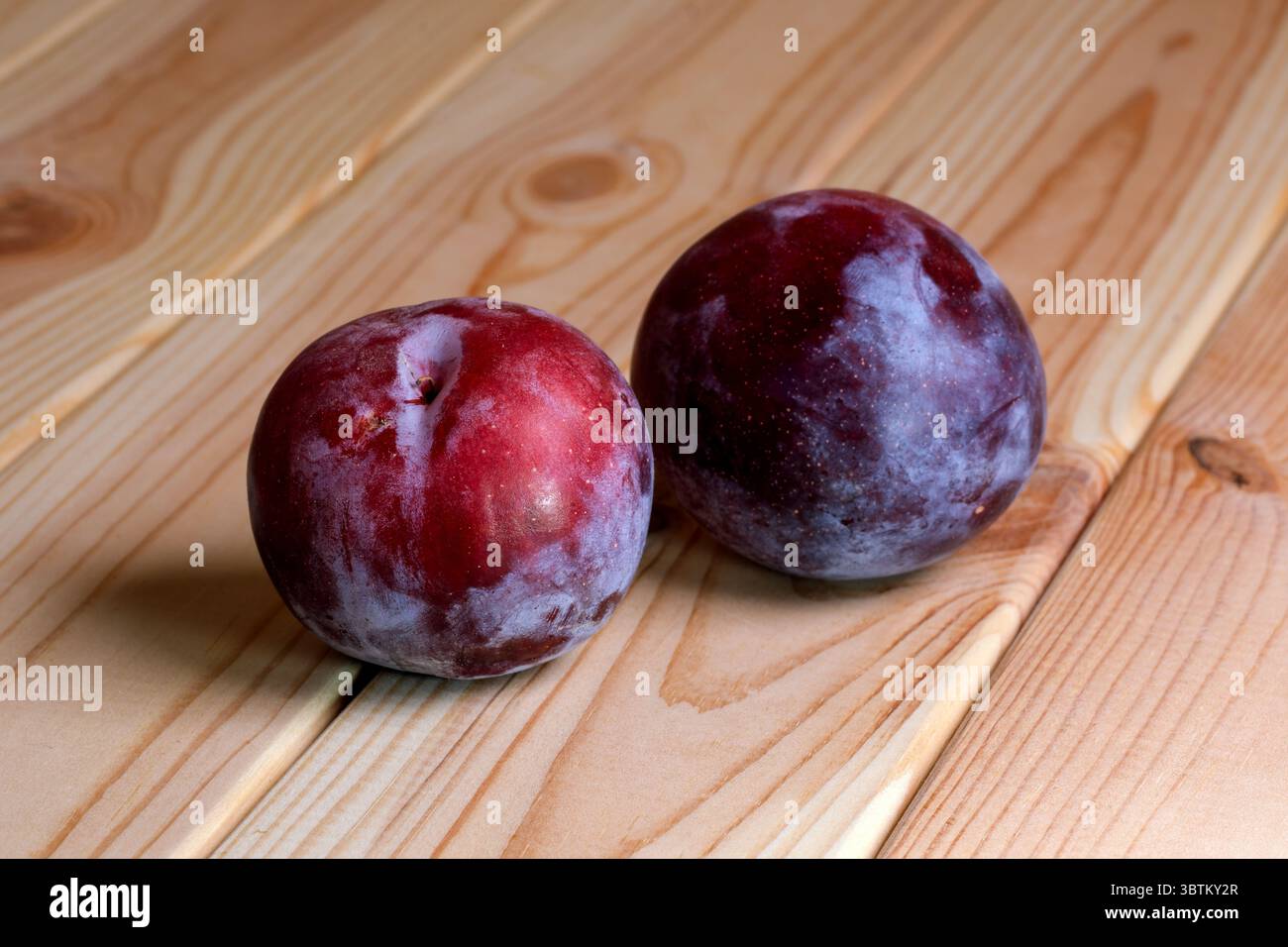 Deux prunes mûres douces rondes non lavées avec de la cire naturelle sur une table en bois clair gros plan Banque D'Images