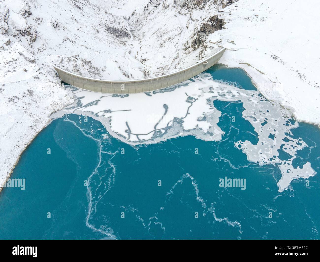 Vue aérienne d'un barrage retenant les eaux turquoises glacées sur fond de montagnes recouvertes de neige, Anniviers, Valais, Suisse. Banque D'Images