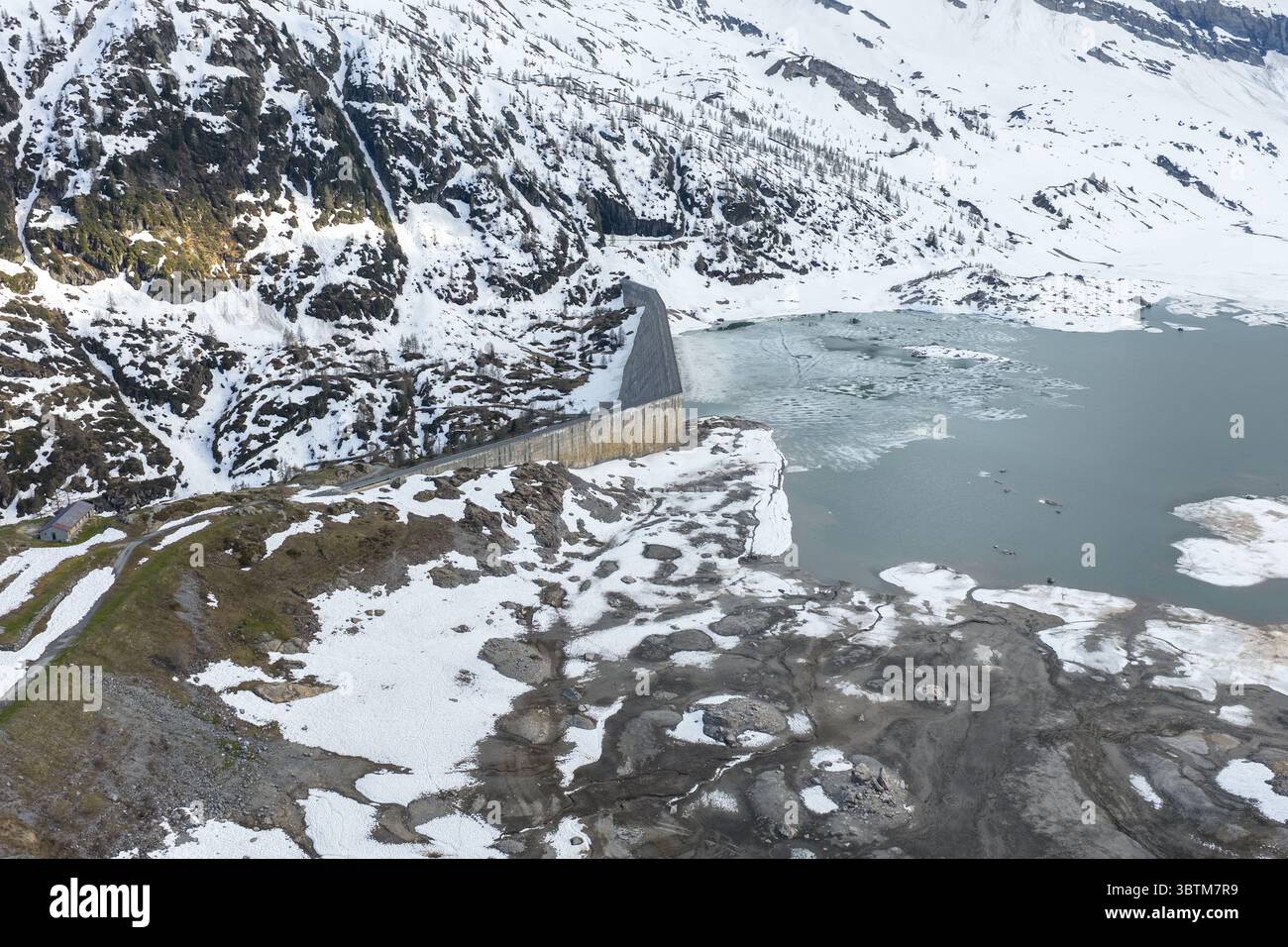 Vue aérienne d'un barrage retenant un lac glaciaire, avec des montagnes enneigées en arrière-plan, Saint-Maurice, Valais, Suisse. Banque D'Images