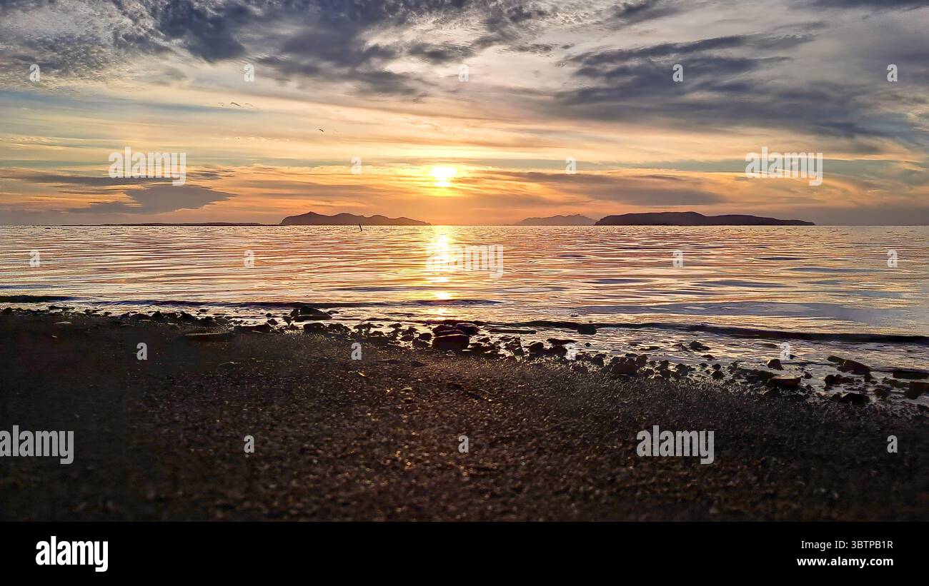 Coucher de soleil sur la mer près de Paceco, Trapani, Sicile, avec silhouette d'îles à l'horizon et vagues calmes sur une plage rocheuse. Banque D'Images