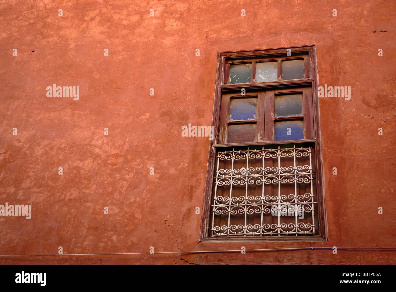 Vieille fenêtre en bois avec des barres métalliques sur un mur en stuc rouge. Détail architectural d'un bâtiment traditionnel. Banque D'Images
