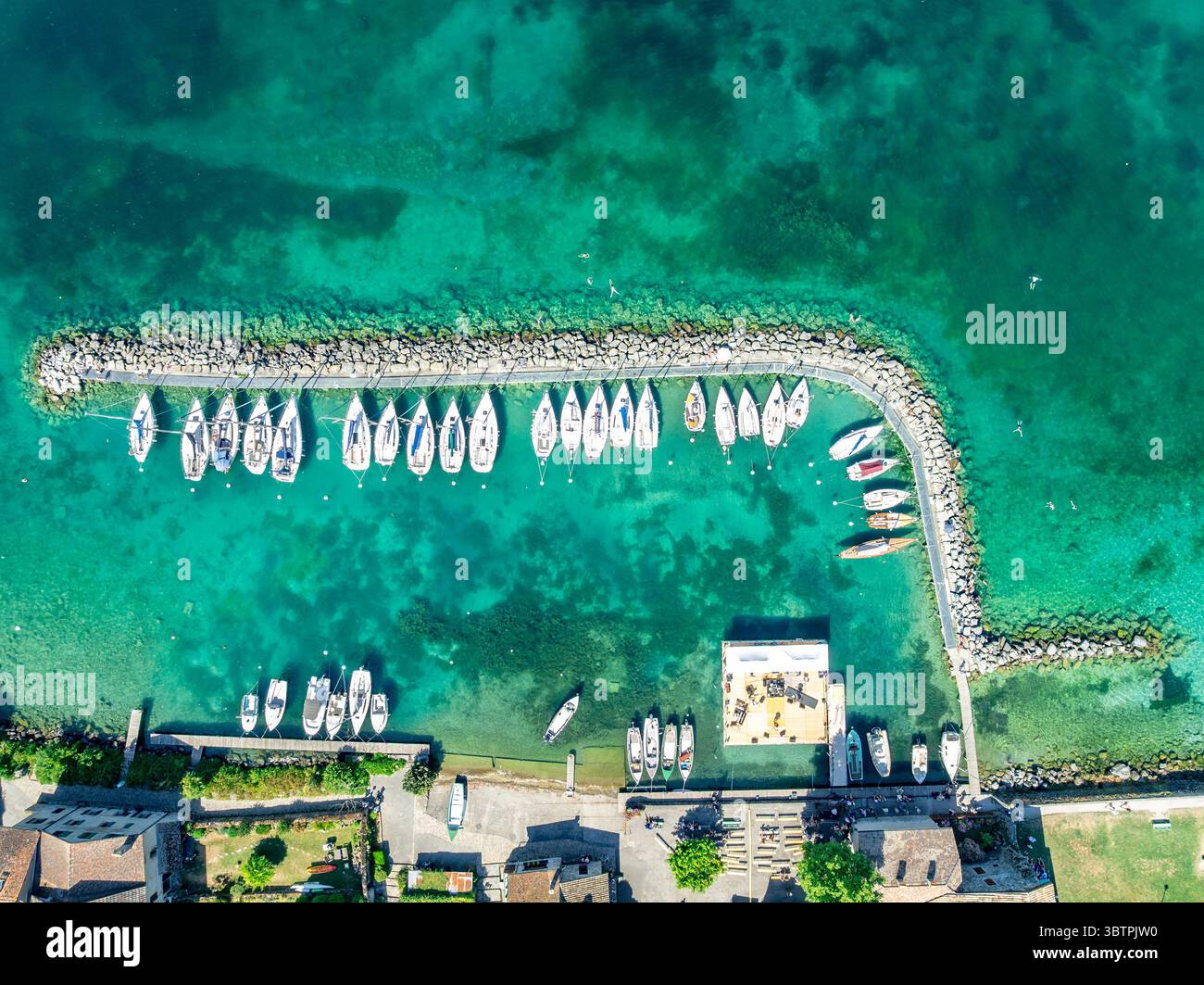Vue aérienne de haut en bas de voiliers blancs amarrés en forme de croissant dans un port d'eau turquoise à Yvoire France Banque D'Images