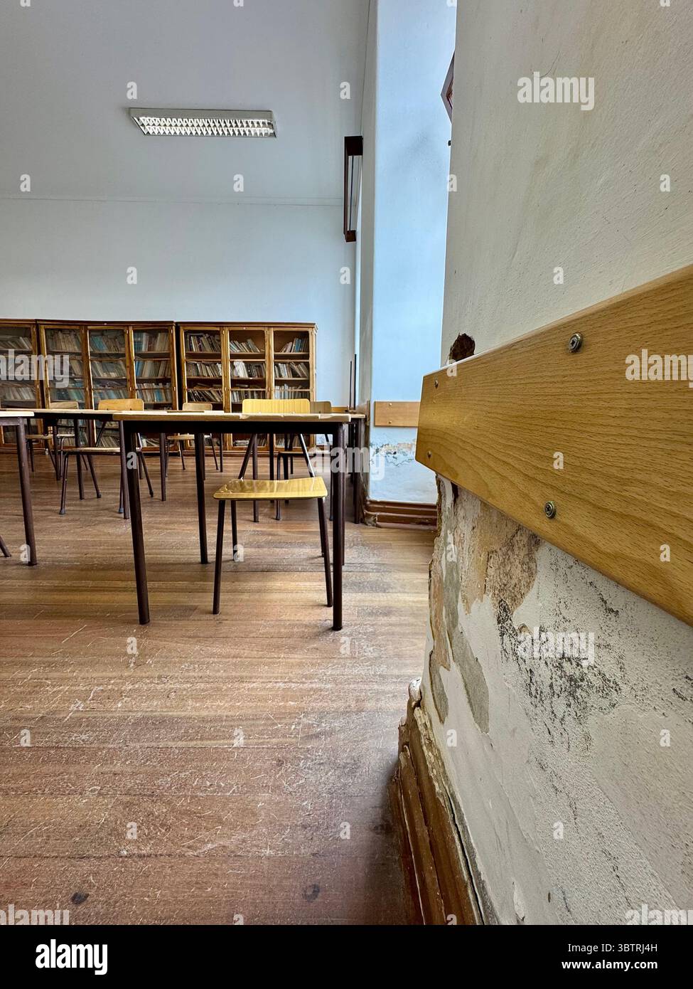 Ancienne salle de classe avec des bureaux en bois et des dommages visibles aux murs, intérieur de l'école Banque D'Images