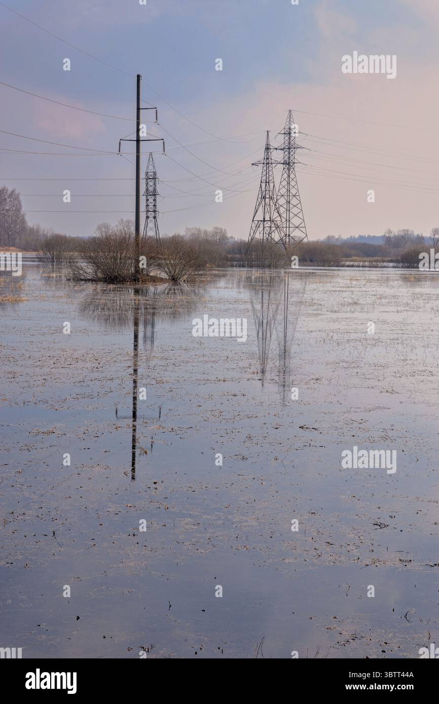 Tours électriques reflétées dans les eaux de crue sur un terrain rural calme sous un ciel nuageux - une image frappante de la nature et de la tension des infrastructures Banque D'Images