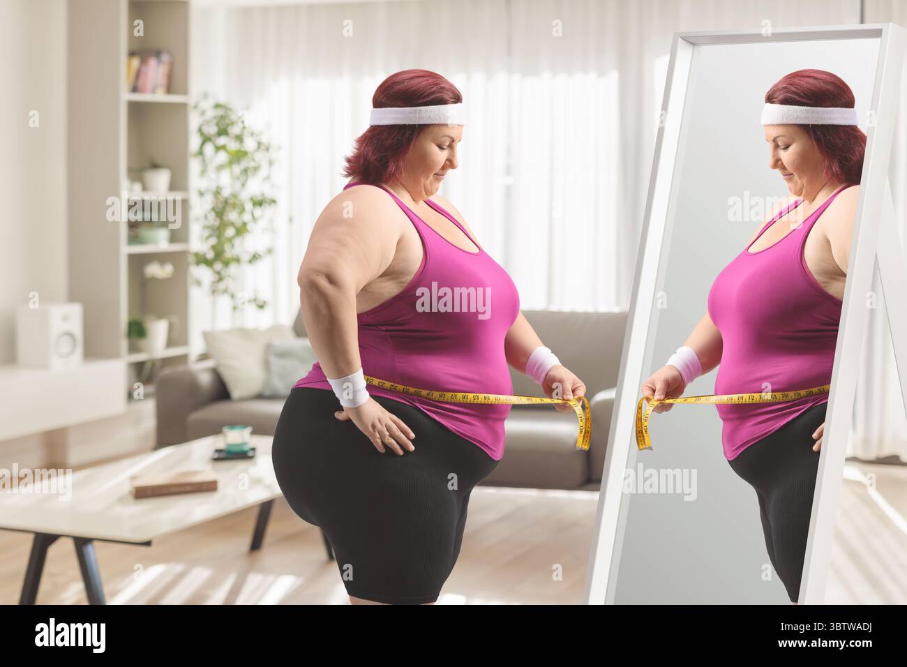 Femme en surpoids tenant un ruban à mesurer devant un miroir Banque D'Images