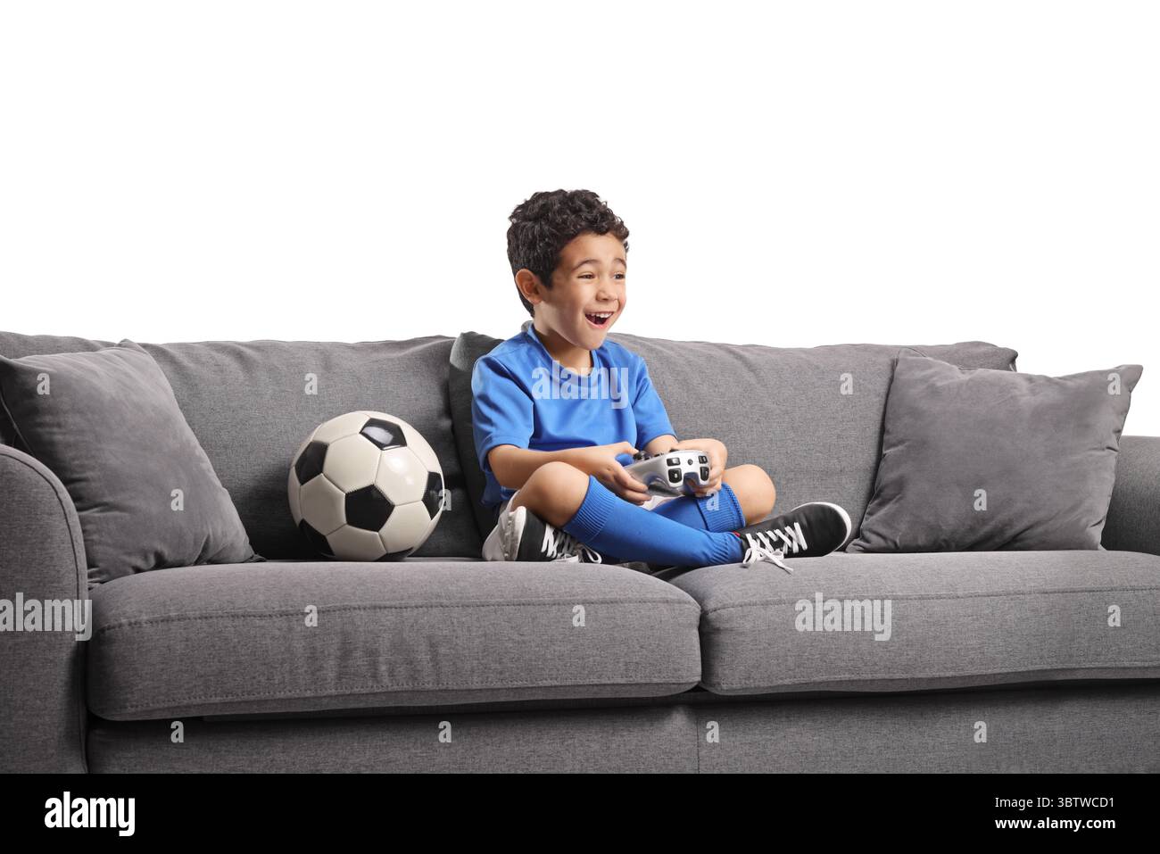 Garçon assis sur un canapé avec un ballon de football et jouant à un jeu vidéo isolé sur fond blanc Banque D'Images