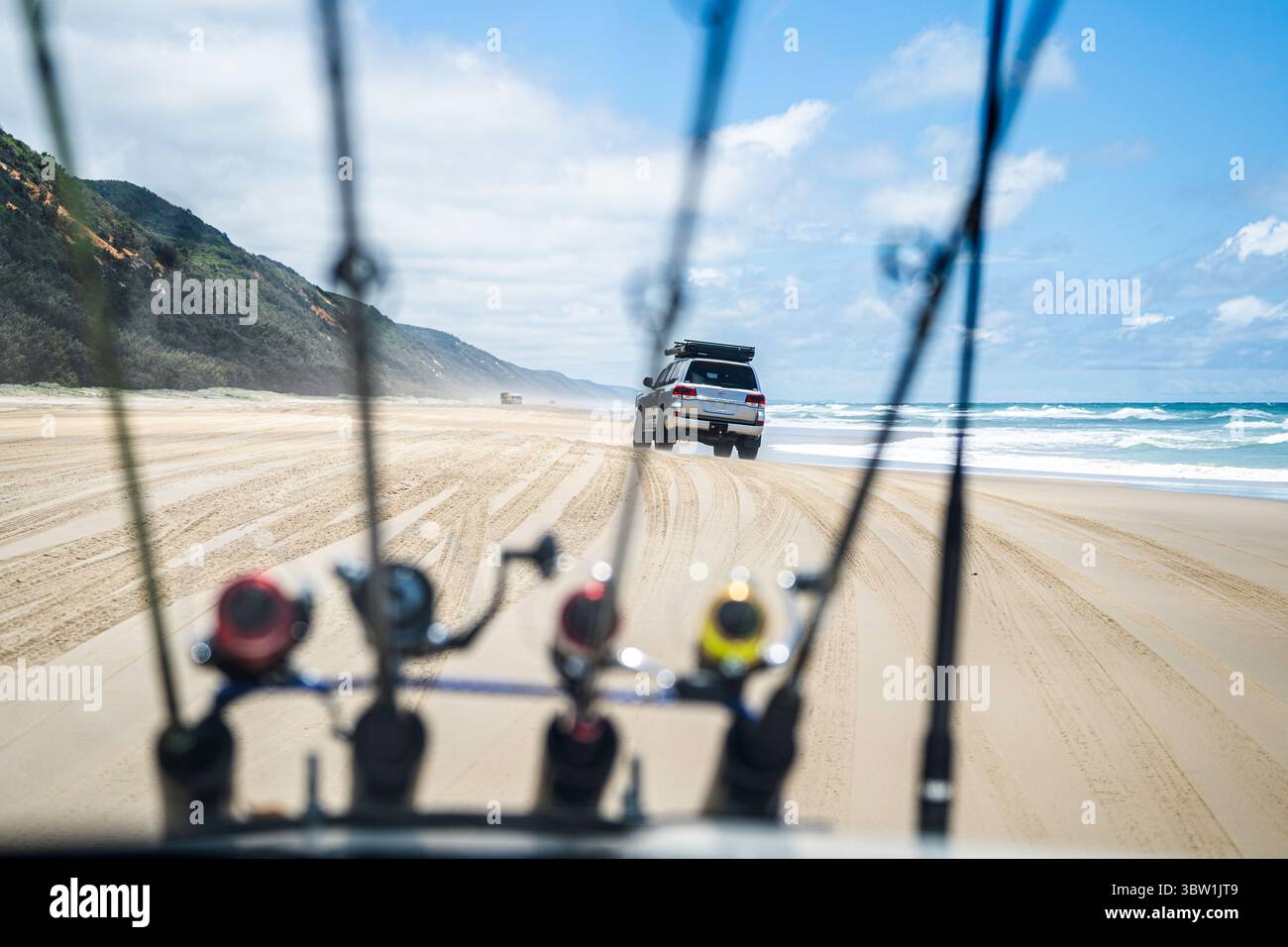 Véhicules 4x4 conduisant sur une large plage de sable vue à travers des cannes à pêche montées sur le capot, Teewah Beach, parc national de Great Sandy, Queensland, Australie Banque D'Images