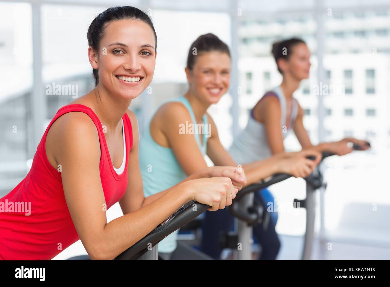 Trois femmes font du vélo dans un studio de fitness design plat avec des fenêtres de la ville et des vélos d'exercice Banque D'Images