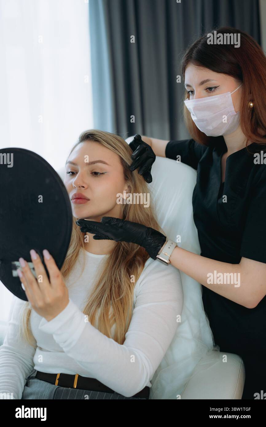 femme médecin esthétique à la consultation personnalisée anti-âge avec une jeune cliente tenant un miroir Banque D'Images