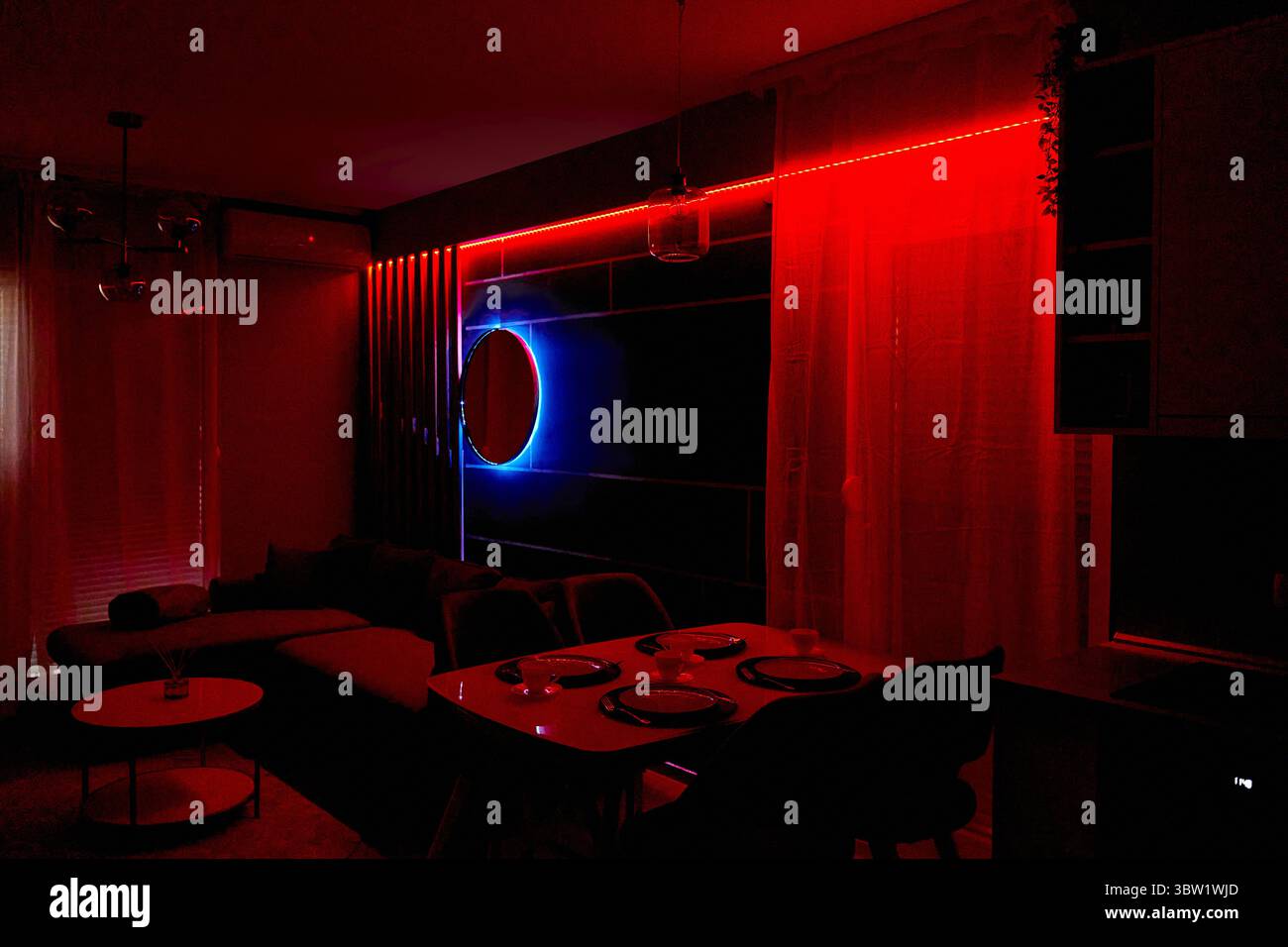 Un salon élégant dispose d'un éclairage LED rouge et bleu, un mur d'accent miroir, un canapé confortable et un ensemble de table à manger, créant un at moderne et accueillant Banque D'Images