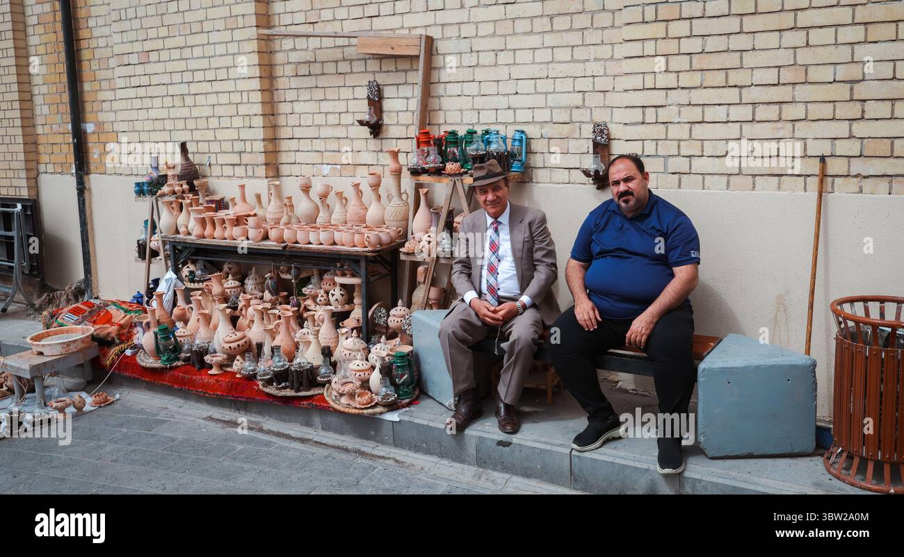 Deux artisans sont assis à côté de leur poterie artisanale dans une rue animée du marché de Bagdad, mettant en valeur l'artisanat local. Banque D'Images