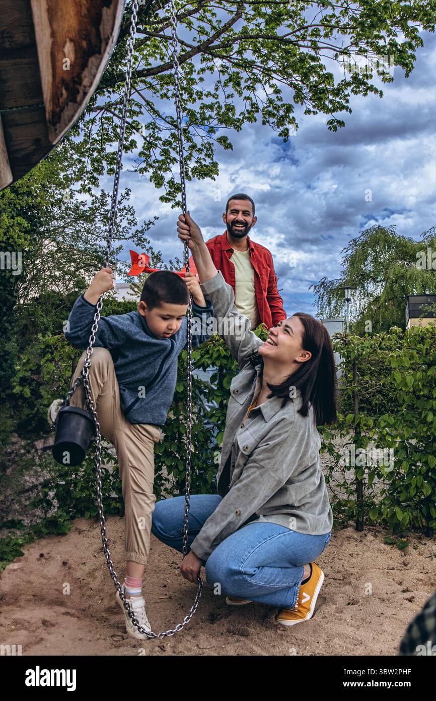 Famille multinationale avec garçon de 6 ans jouant ensemble à l'aire de jeux. Parents impliqués dans la parentalité active, construisant de solides relations avec les enfants Thr Banque D'Images
