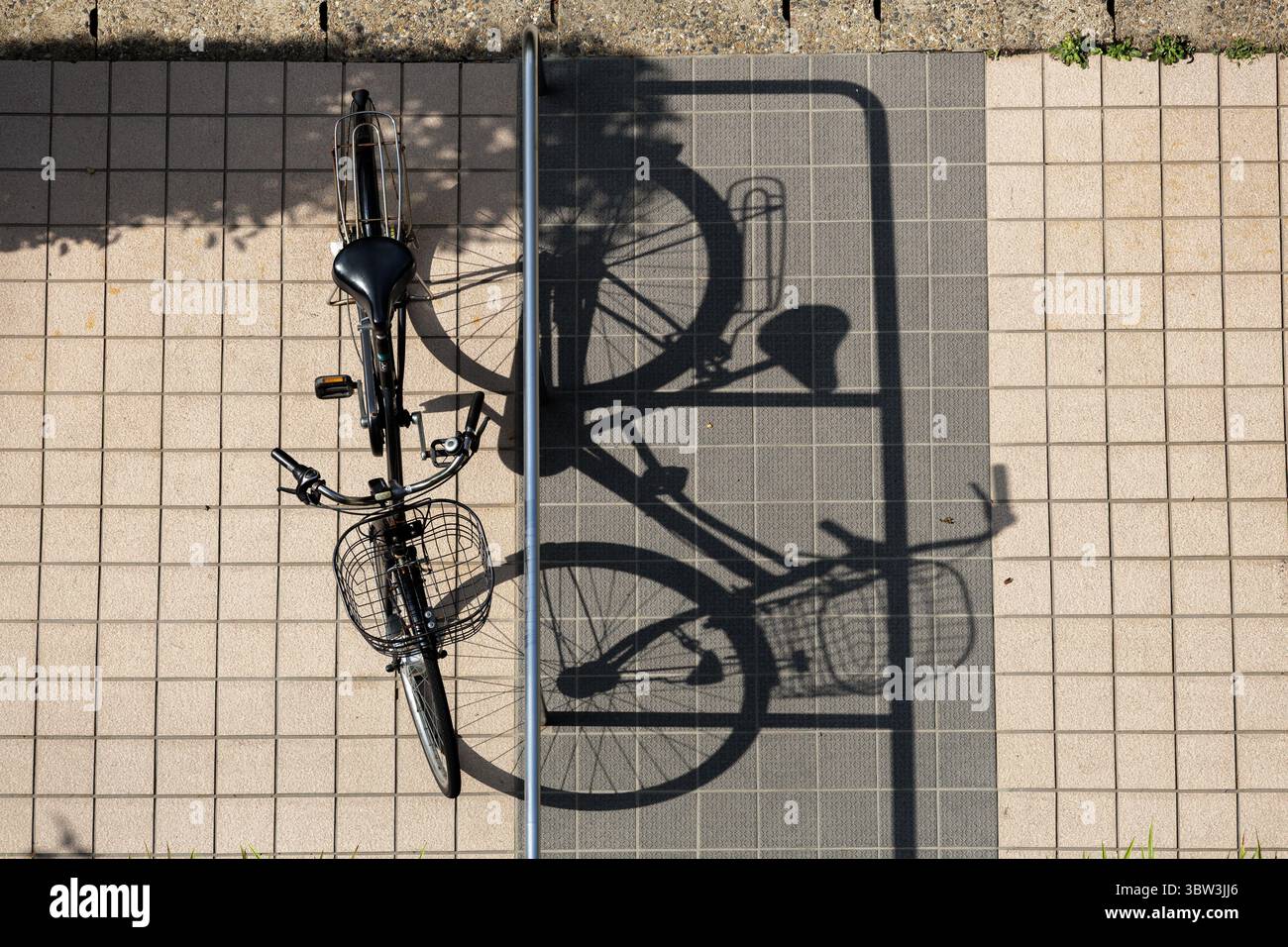 Œil d'oiseau de vélo garé sur un trottoir carrelé, projetant une longue ombre dans la lumière du soleil en fin d'après-midi. La rampe argentée sépare la zone entre le vélo et l'ombre. Banque D'Images