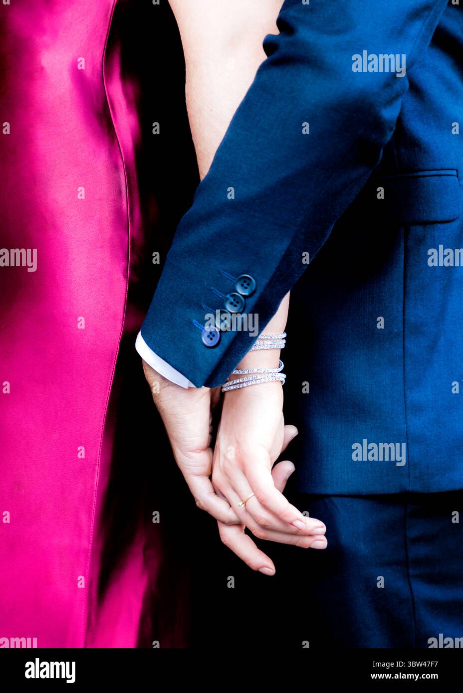 Un couple se tient la main, la femme portant une bague et des bracelets, et l'homme portant un costume bleu. Banque D'Images