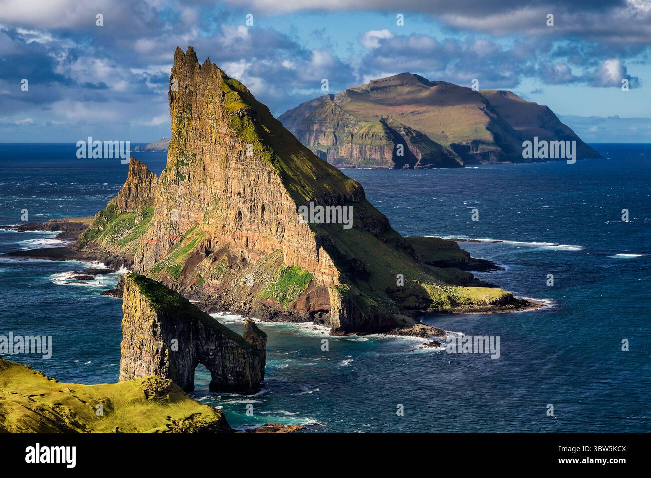 Vue sur la pile de la mer de Drangarnir et l'îlot Tindhólmur s'élèvent majestueusement de l'Atlantique Nord, falaises déchiquetées contrastant avec la mer bleue sereine, Vágar, îles Féroé. Banque D'Images