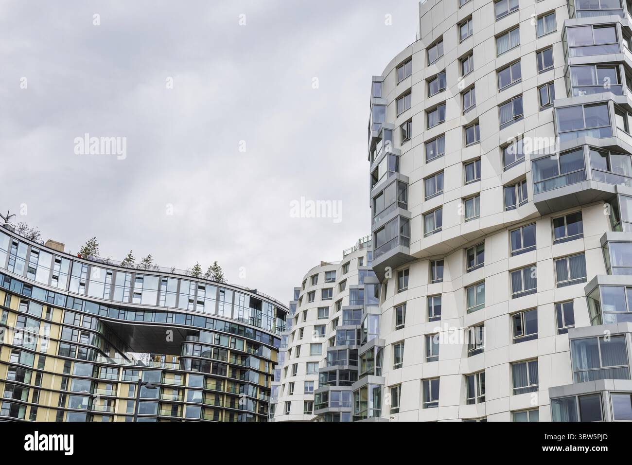Image présentant des bâtiments modernes courbes avec des façades blanches et de vastes vitrages, posés contre un ciel urbain nuageux dans un style architectural contemporain Banque D'Images