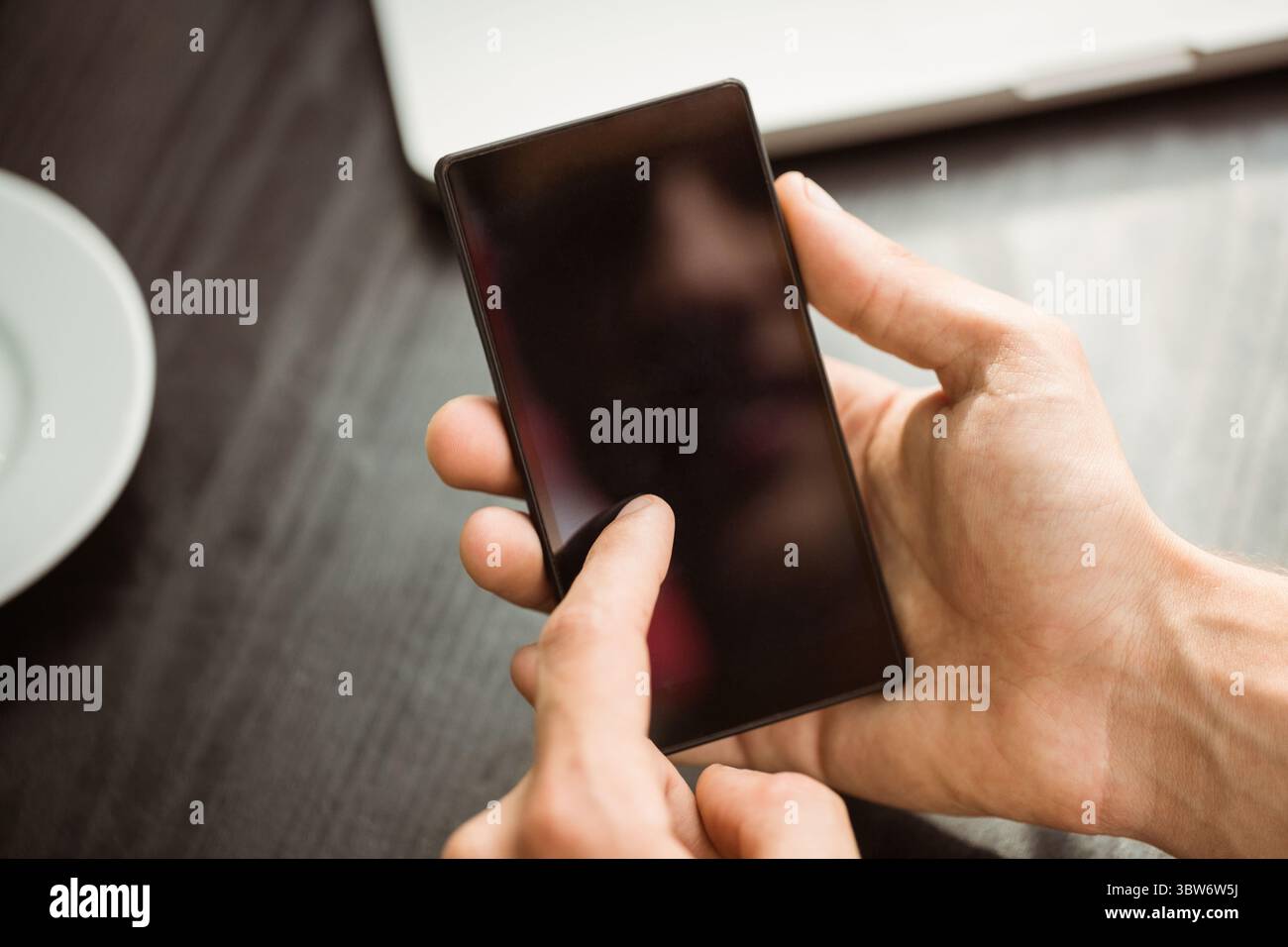 Les mains tiennent le smartphone dans un plan de table en bois sombre plat gros plan, avec ordinateur portable et plaque Banque D'Images Les mains tiennent le smartphone dans un plan de table en bois sombre plat gros plan, avec ordinateur portable et plaque Banque D'Images