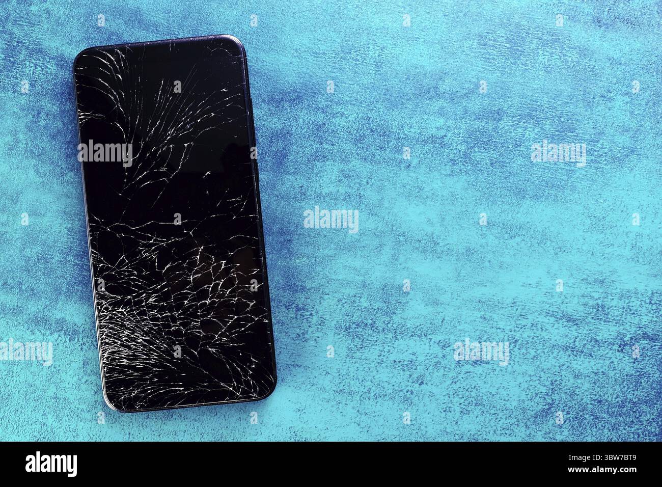 Un téléphone noir avec un écran cassé repose sur un fond texturé turquoise. Fond pour la publicité de services sur la réparation de smartphones avec espace Banque D'Images