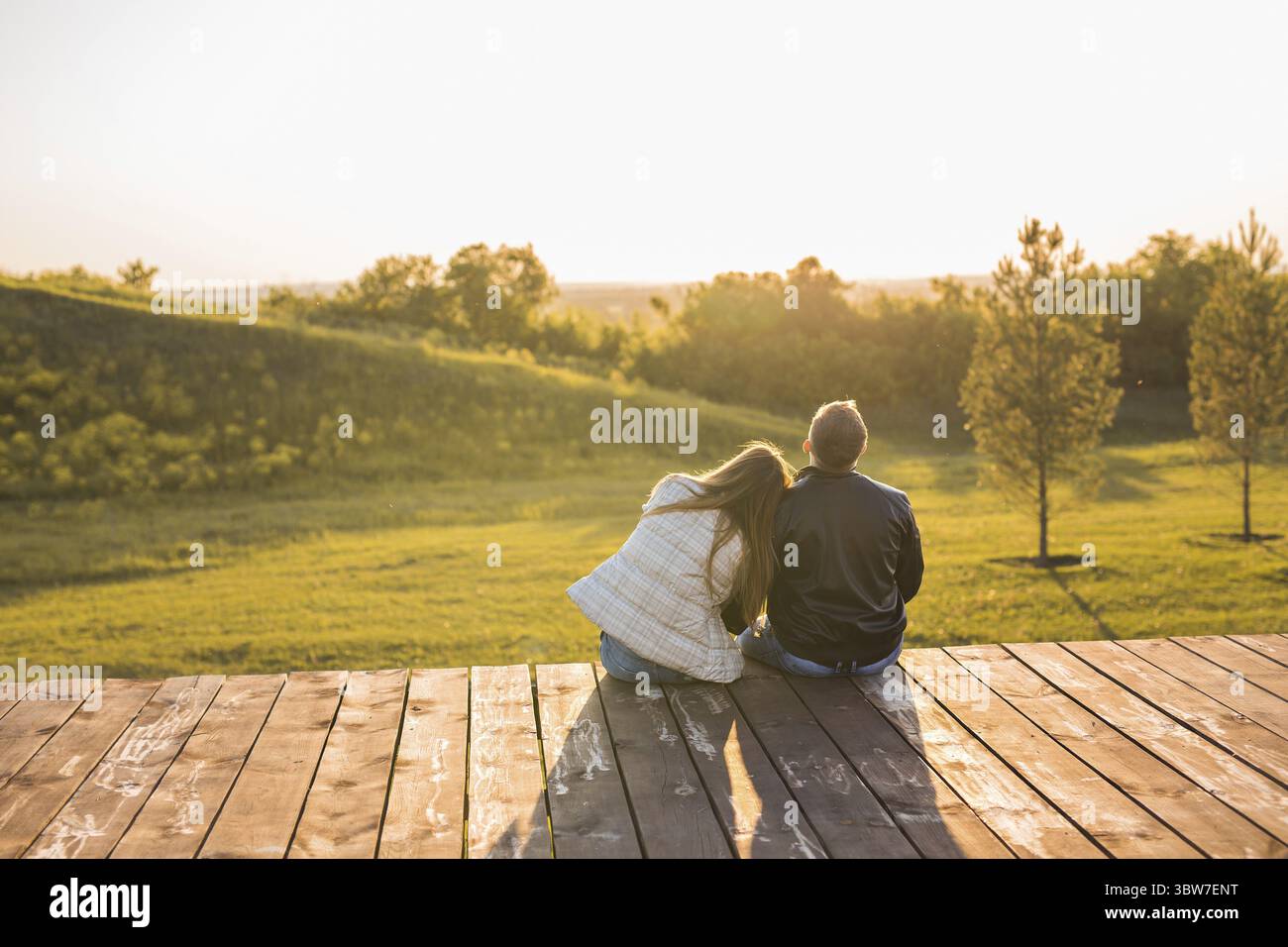 Romantique jeune couple profitant d'une date assis dans une étreinte proche sur un banc de parc donnant sur un lac, vue de derrière Banque D'Images