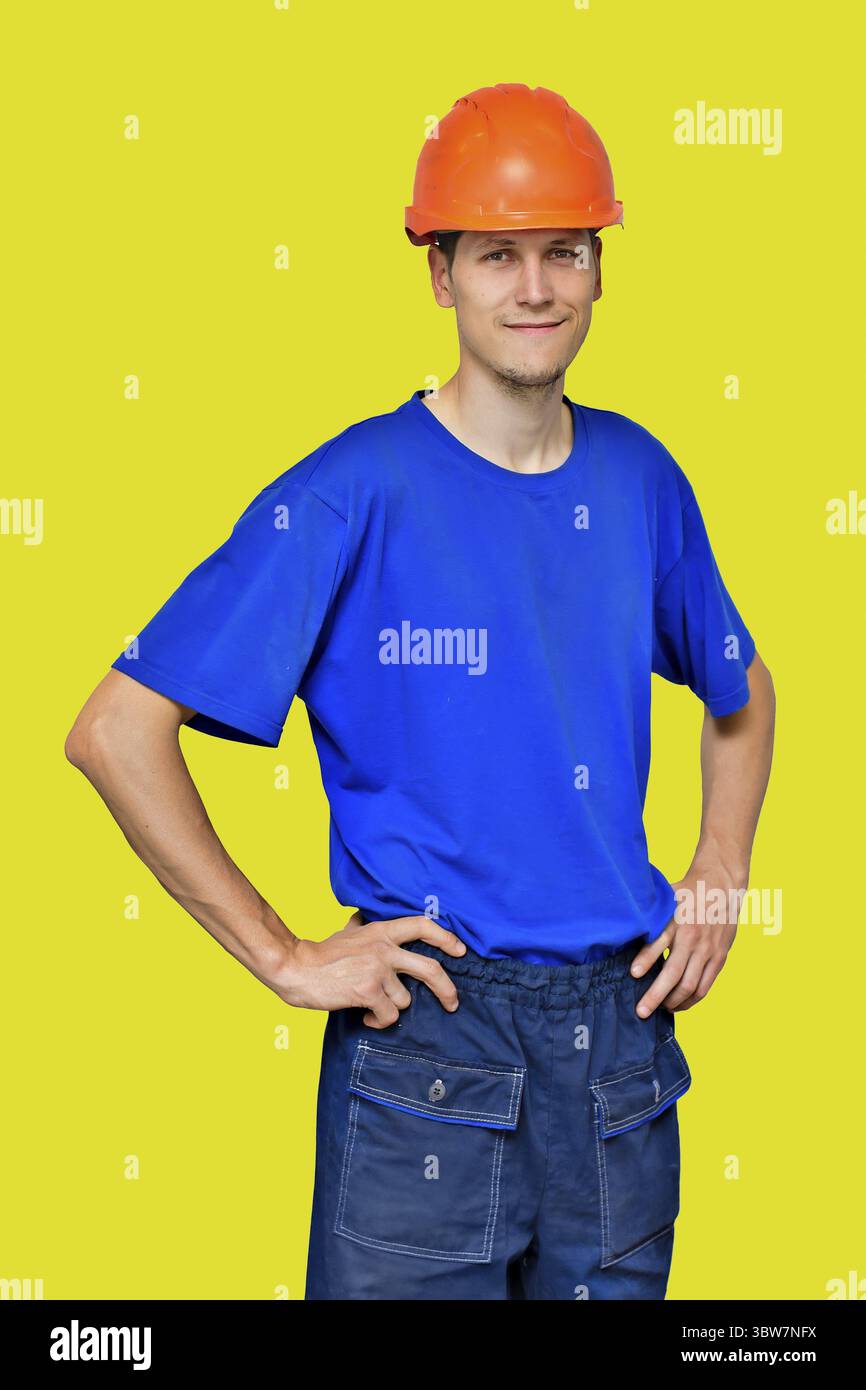 Portrait d'un jeune bel homme dans un casque de construction et des vêtements de travail isolés sur un fond jaune. Un ouvrier manuel positif Banque D'Images