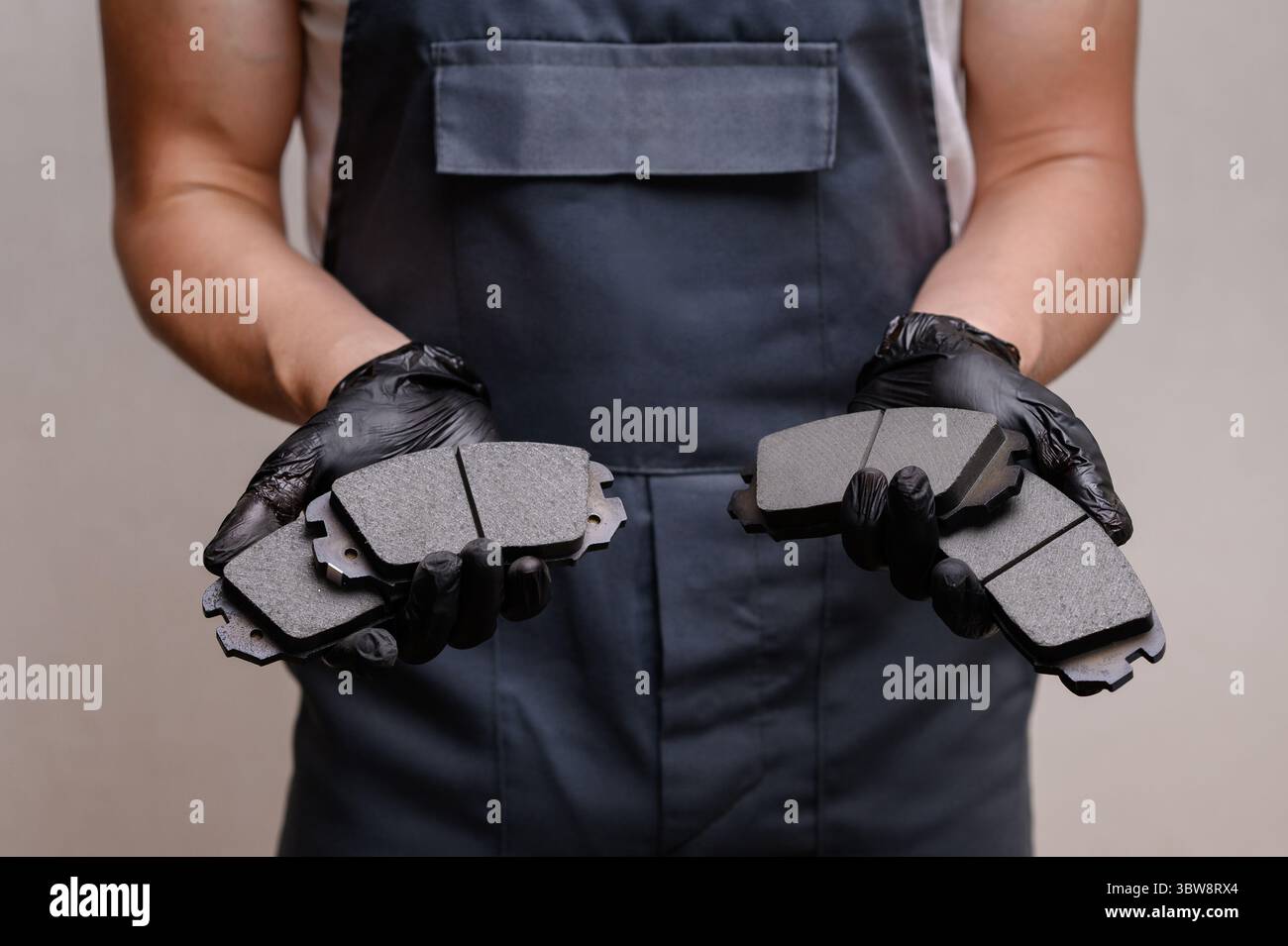 Mécanicien automatique en combinaison tenant quatre plaquettes de frein dans les mains, gros plan, se préparant à les remplacer. Concept d'entretien, facilité d'entretien du système de frein de voiture Banque D'Images