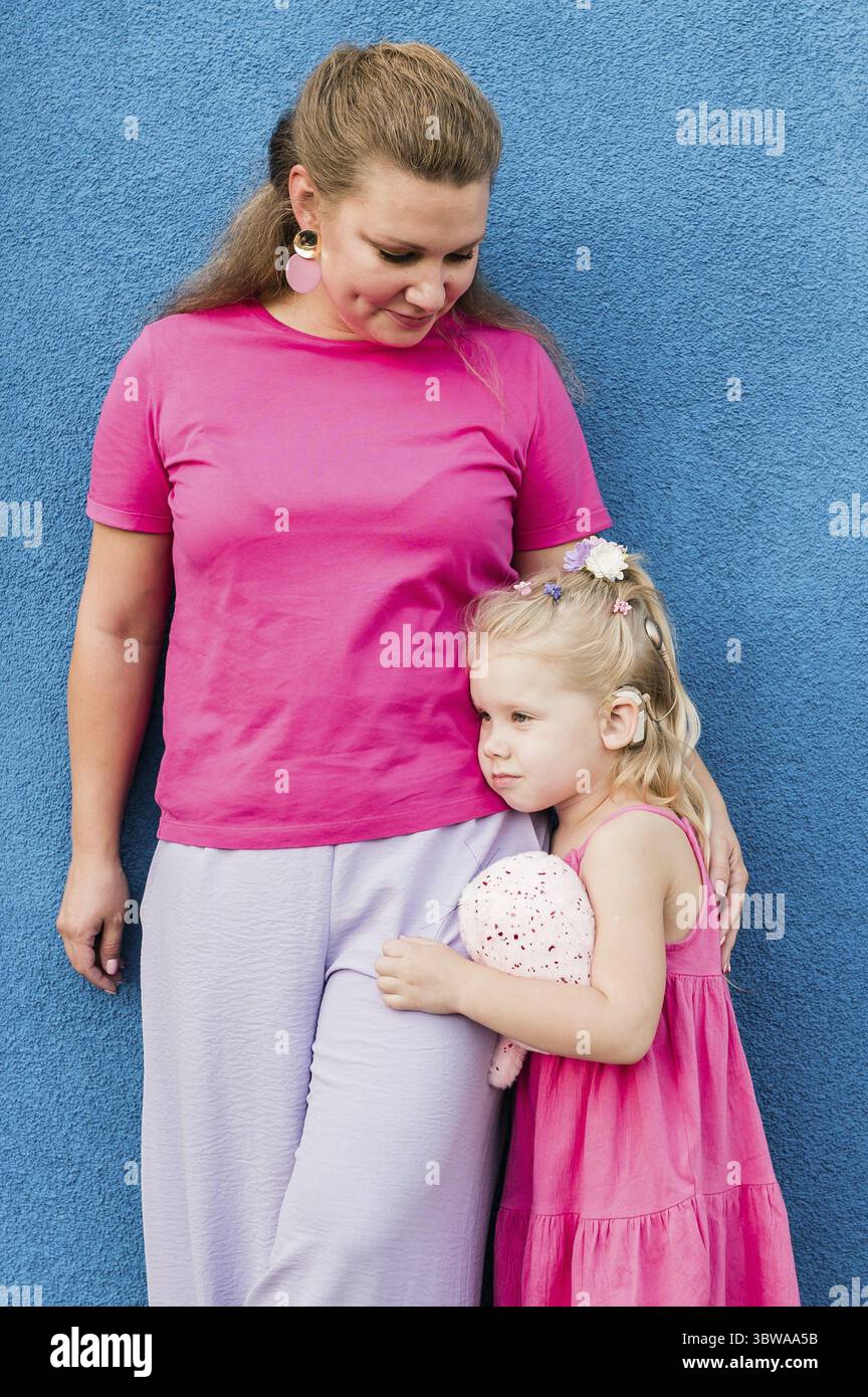 Blondes kleines Maedchen mit cochlea Implantat spielen mit ihrer Mutter im Freien. Hoeren Beeintraechtigung taub und Gesundheit Konzept. Vielfalt und Banque D'Images