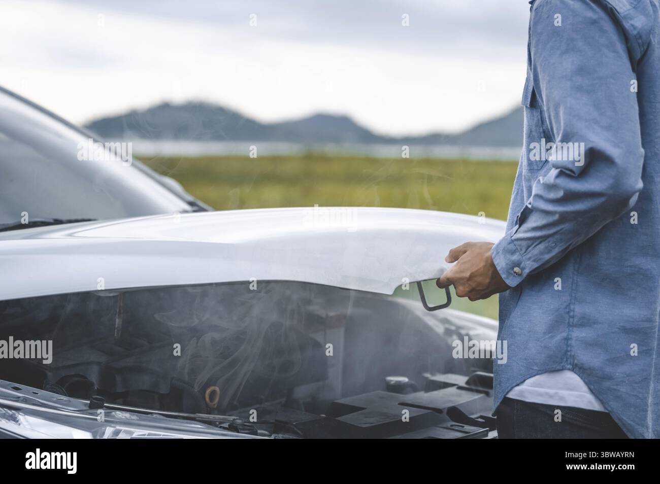 Homme asiatique ouvrir le capot de voiture pour la réparation comme service d'entretien avec fond de paysage entre le long voyage de route. Voiture cassée et panne dans meado de montagne Banque D'Images