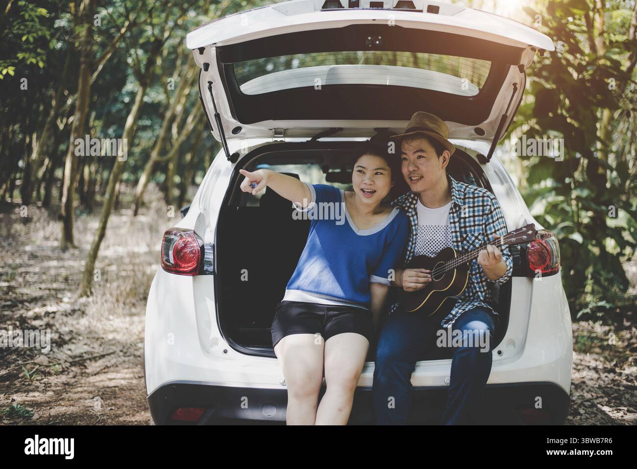 Couple asiatique pointant et voyageant dans la forêt en voiture, amoureux des musiciens. Concept aventure et plein air. Thème nature et style de vie. Thème Road trip Banque D'Images