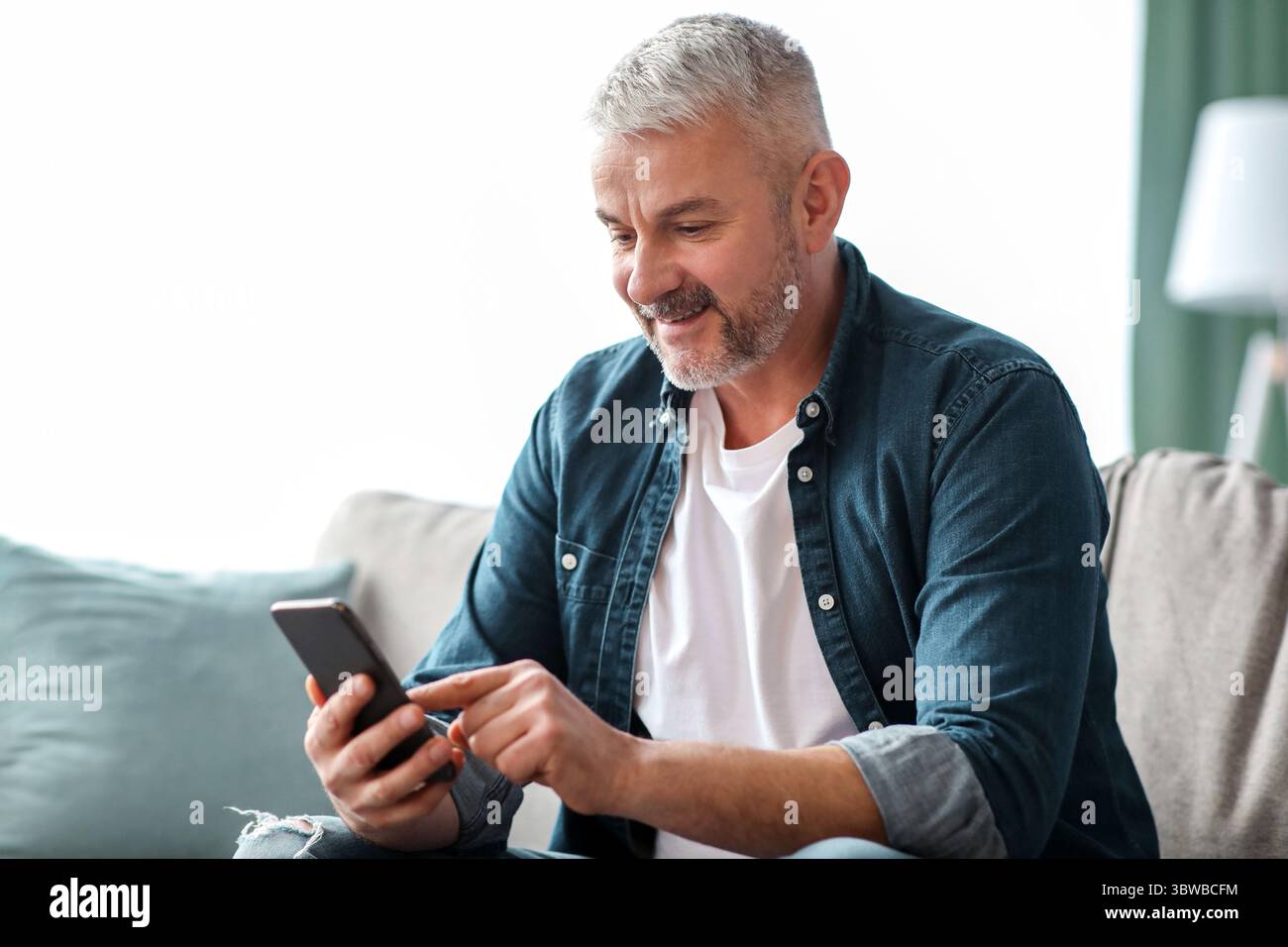 Homme senior souriant utilisant un smartphone à la maison Banque D'Images