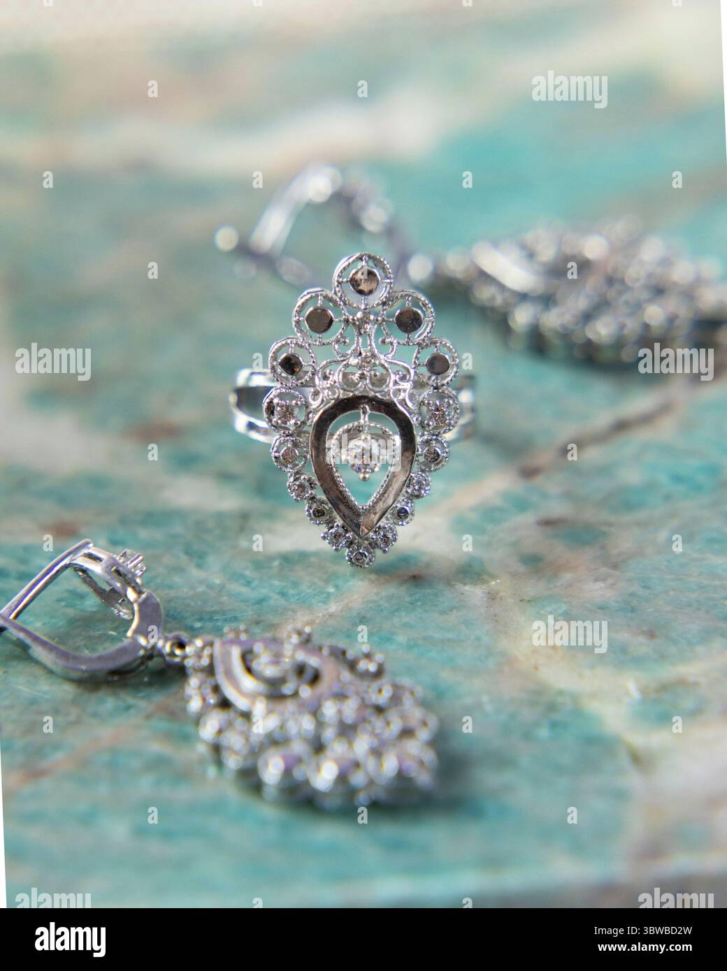 Bague et boucles d'oreilles en argent avec un design orné étincelant sur une surface turquoise Banque D'Images