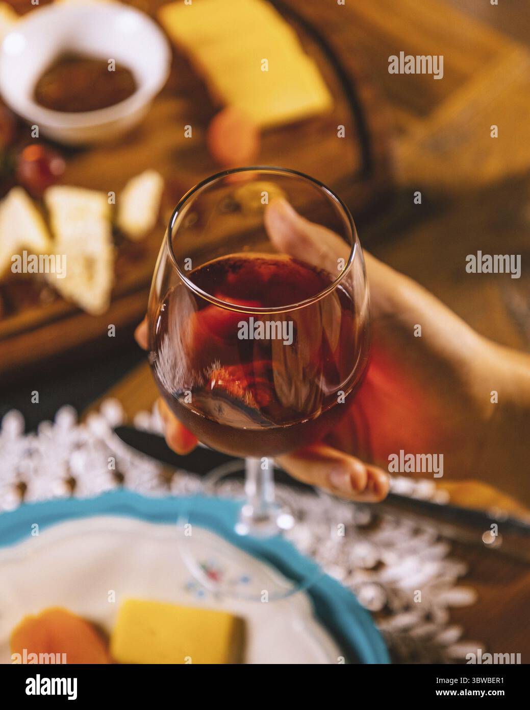 Femme tenant un verre de vin rouge avec une planche à fromage avec des raisins et du miel en arrière-plan Banque D'Images
