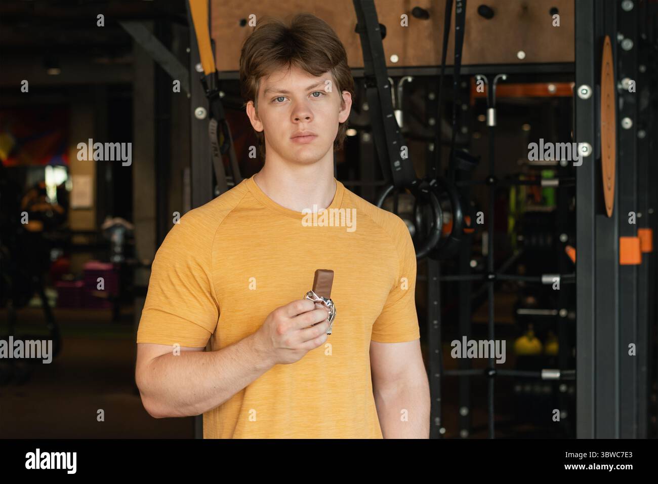 Bodybuilder ou jeune homme mangeant barre d'énergie. Encas musclés pour sportifs barre protéinée tout en se reposant après une séance d'entraînement au gymnase ou au centre de fitness. Banque D'Images