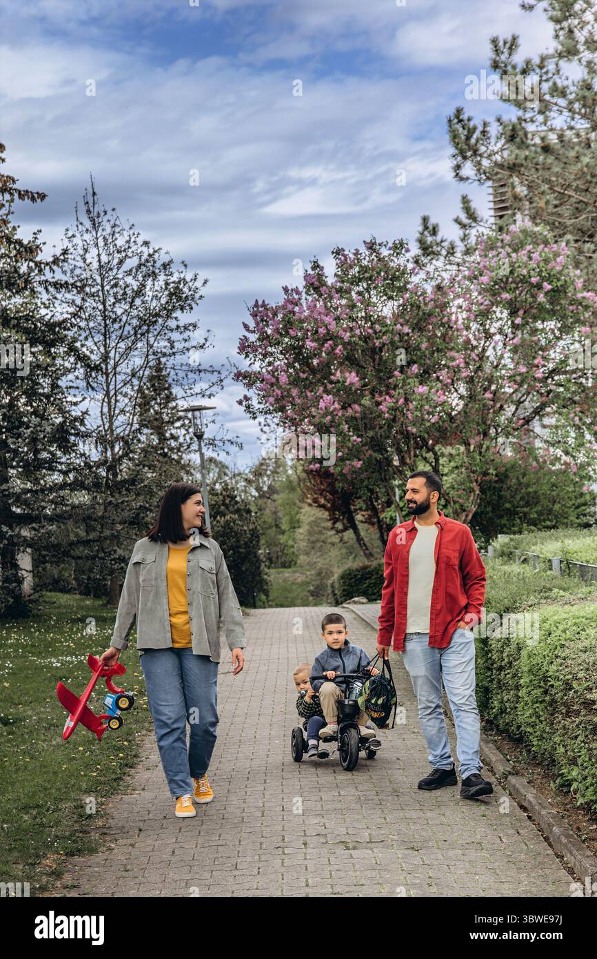 Famille avec deux garçons à vélo et parents marchant à proximité dans un parc. Plaisir en plein air, liens, amour et bonheur. Activité week-end dans la nature avec Banque D'Images