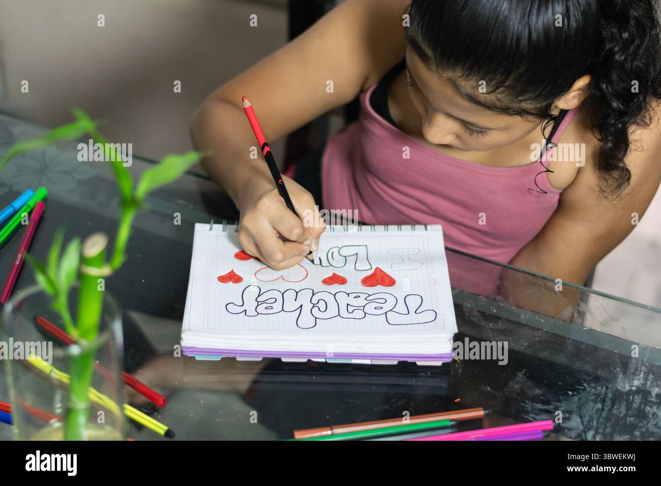 Petite fille colombienne se coloriant soigneusement dans son cahier sur une table en verre. Peindre avec ses couleurs Banque D'Images