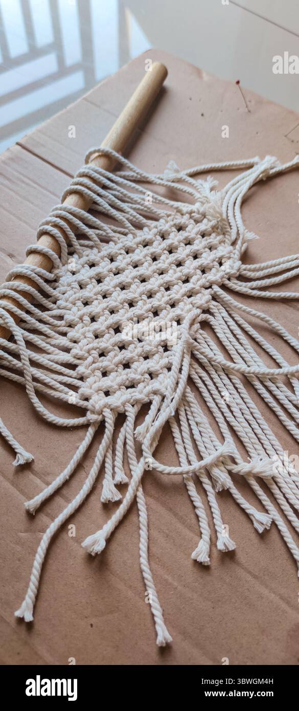 Accrochage mural macramé fait à la main en cours. Une belle pièce de macramé en cours, confectionnée avec une corde de coton naturel sur une cheville en bois. Le kn complexe Banque D'Images