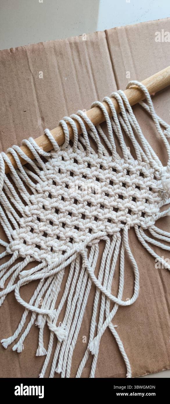 Accrochage mural macramé fait à la main en cours. Une belle pièce de macramé en cours, confectionnée avec une corde de coton naturel sur une cheville en bois. Le kn complexe Banque D'Images