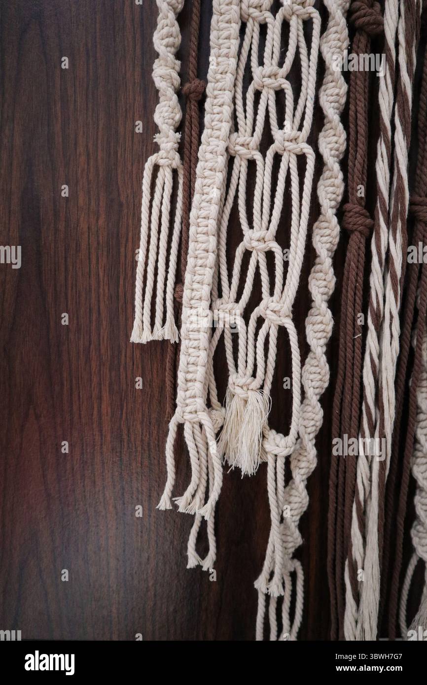 Gros plan d'une suspension murale en macramé aux tons neutres avec des nœuds complexes et une cheville en bois, sur fond de bois sombre Banque D'Images