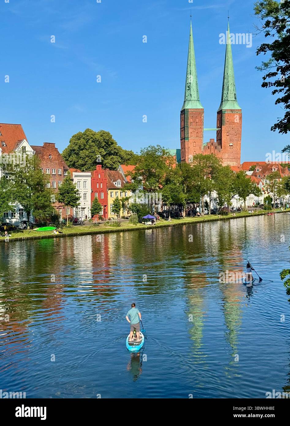 Les gens paddleboard sur la rivière Trave à Lübeck, en Allemagne, avec les tours jumelles emblématiques de l'église de Marie et des bâtiments historiques le long de l'eau - Image de stock capturée avec un smartphone